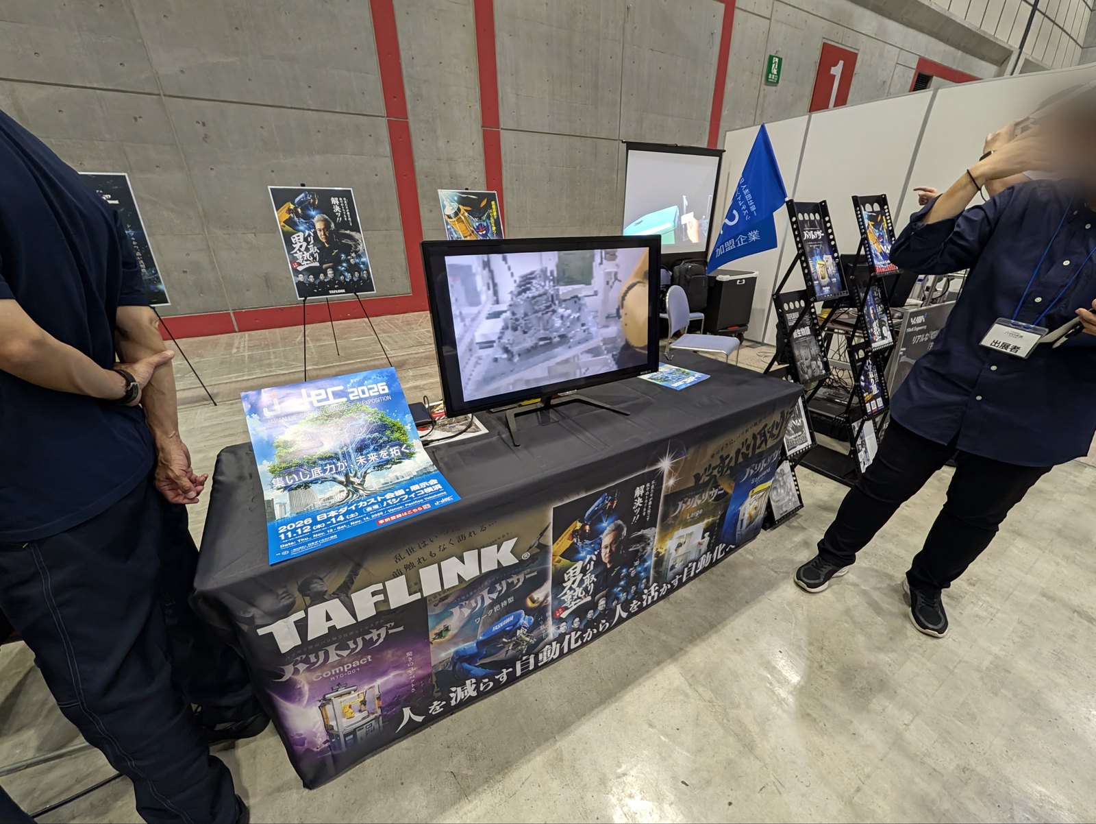 TAFLINKのブース。テーブルクロスに「人を減らす自動化から人を活かす自動化へ」とある